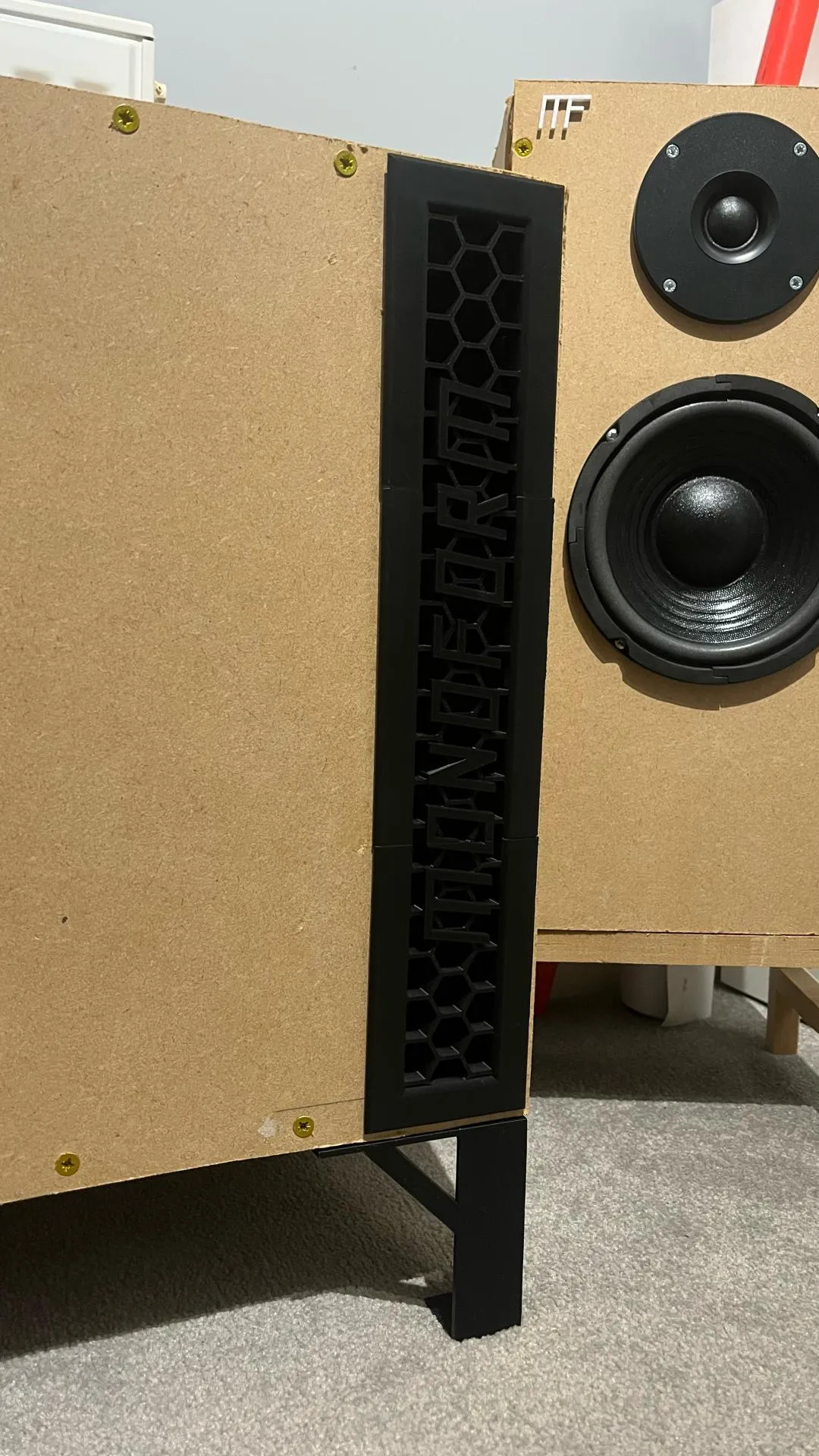Rectangular subwoofer port with a black grille beside a two-way speaker