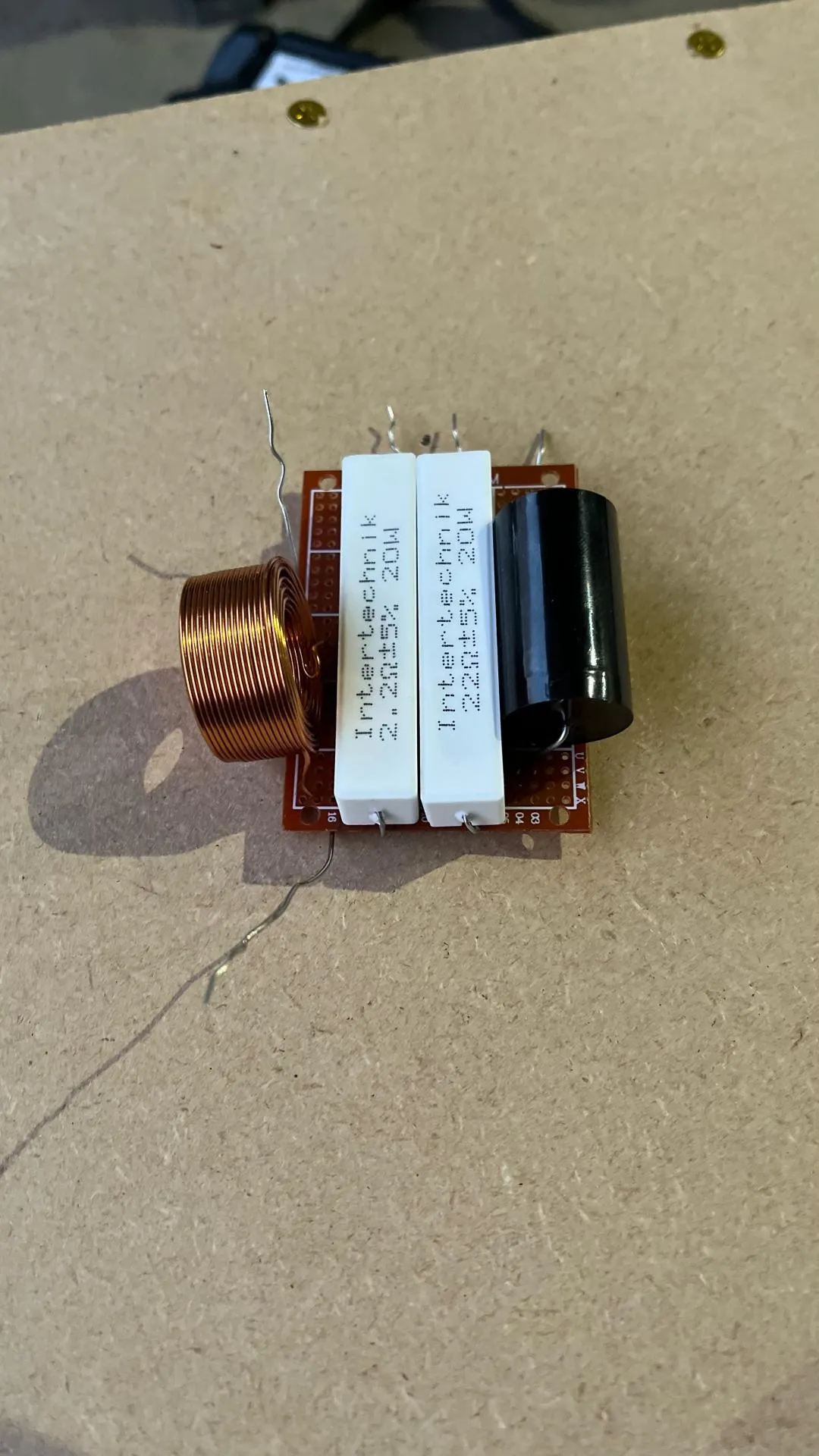 Passive crossover board with a copper coil, two white resistors and a black capacitor